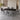 tiaroのブラック・ライン柄のセラミックダイニングテーブルとグレーのチェア6脚。角を丸めた薄い長方形天板、ブラックの四本脚、すっきりした食卓の形状を、自然光の落ち着いた壁と床のあるモダンなダイニングで見せる室内写真。